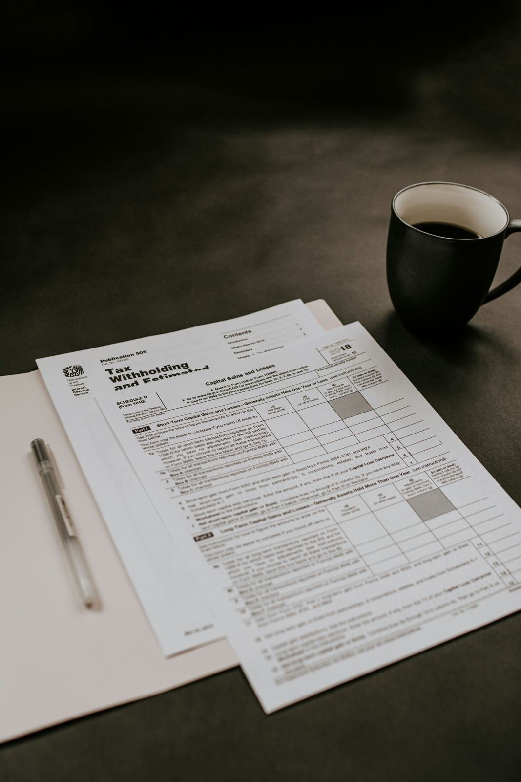 Tax and business filing forms on a desk with a pen and coffee